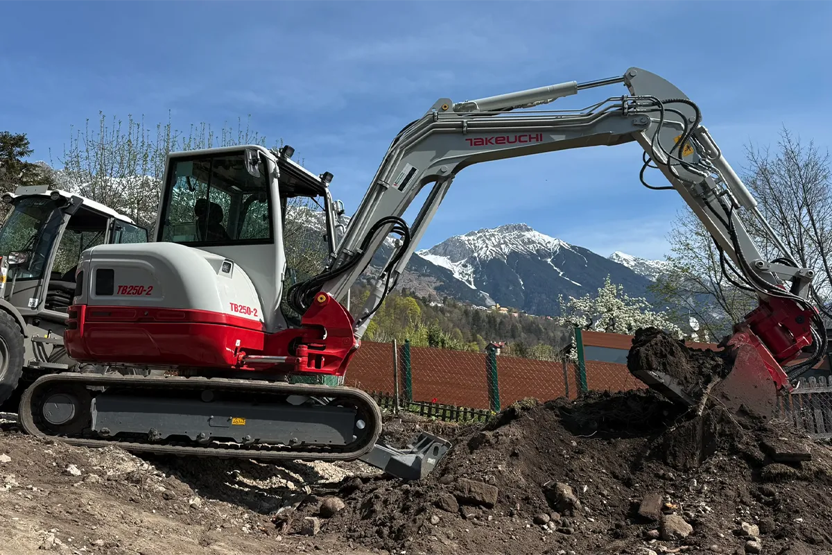 Minibagger bei Erdarbeiten auf einer Baustelle in Tirol mit Bergkulisse Minibagger bei Erdarbeiten auf einer Baustelle in Tirol mit Bergkulisse